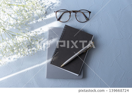 A natural desk image featuring baby's breath, a notebook, and glasses. A natural desk image featuring baby's breath, a notebook, and glasses. 139668724
