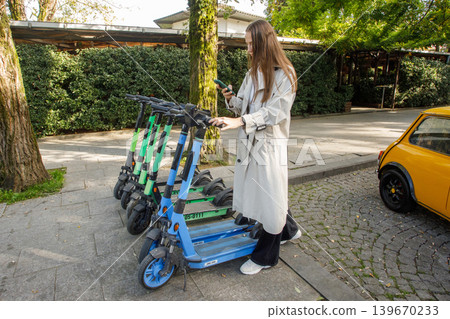 Young woman rents electric scooter with her cell phone. Woman uses an app on her smartphone Young woman rents electric scooter with her cell phone. Woman uses an app on her smartphone 139670233
