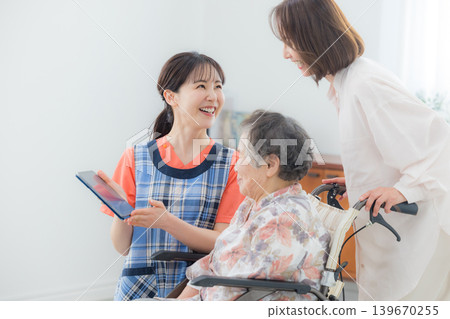 一位護理人員正在使用平板電腦,一位老人坐在輪椅上。 一位護理人員正在使用平板電腦,一位老人坐在輪椅上。 139670255
