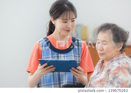 一位護理人員正在使用平板電腦,一位老人坐在輪椅上。 一位護理人員正在使用平板電腦,一位老人坐在輪椅上。 139670263