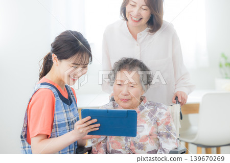 一位護理人員正在使用平板電腦,一位老人坐在輪椅上。 一位護理人員正在使用平板電腦,一位老人坐在輪椅上。 139670269