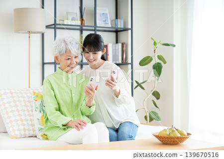 A senior mother and her middle-aged daughter looking at their smartphones in the living room. A senior mother and her middle-aged daughter looking at their smartphones in the living room. 139670516