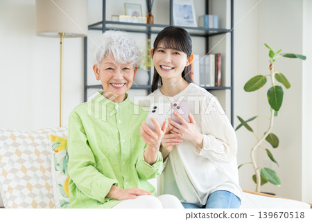 A senior mother and her middle-aged daughter looking at their smartphones in the living room. A senior mother and her middle-aged daughter looking at their smartphones in the living room. 139670518