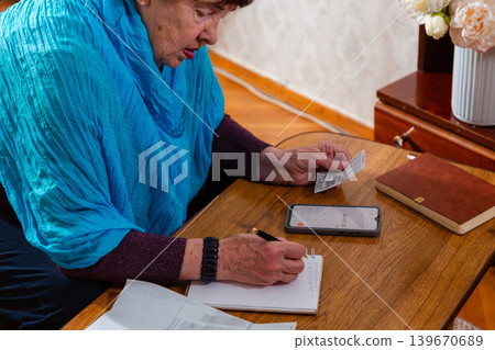 Senior female managing personal budget and tracking expenses indoors. Practical lifestyle and responsibility. Concept of retirement savings and control. Mid shot Senior female managing personal budget and tracking expenses indoors. Practical lifestyle and responsibility. Concept of retirement savings and control. Mid shot 139670689