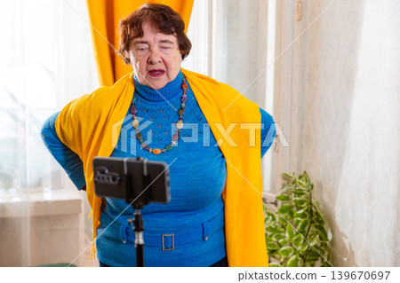 Elderly female doing breathing exercises during livestream. Calm focus and wellness. Concept of senior health. Elderly female doing breathing exercises during livestream. Calm focus and wellness. Concept of senior health. 139670697