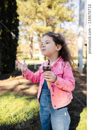 Caucasian little girl holding chocolate ice cream cone and talking in sunny park outdoors. Childhood and summer lifestyle Caucasian little girl holding chocolate ice cream cone and talking in sunny park outdoors. Childhood and summer lifestyle 139670718