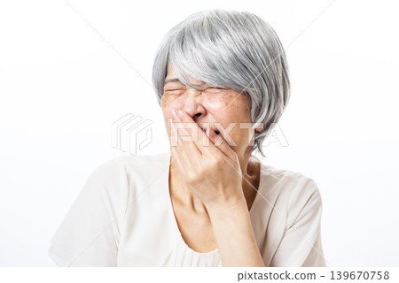 A senior woman covers her mouth with her hand to suppress laughter. A senior woman covers her mouth with her hand to suppress laughter. 139670758