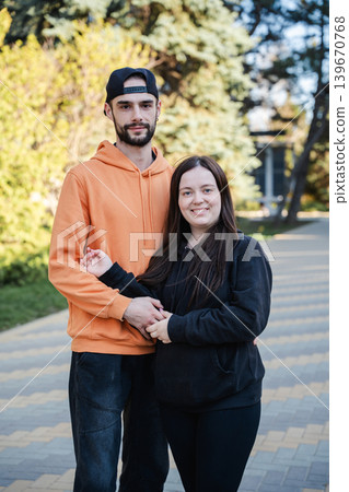 Caucasian husband and wife standing together on park walkway and looking at camera outdoors. Marriage and relationship lifestyle Caucasian husband and wife standing together on park walkway and looking at camera outdoors. Marriage and relationship lifestyle 139670768