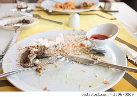 Empty plate with fish bones and sauce on table in restaurant setting 139670809