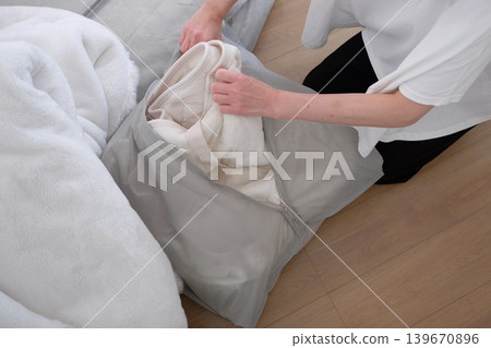 A woman puts her winter comforter into a storage bag. A woman puts her winter comforter into a storage bag. 139670896
