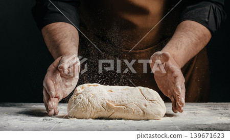 Professional baker shaping fresh dough with flying flour on dark background for artisan bakery advertising concept Professional baker shaping fresh dough with flying flour on dark background for artisan bakery advertising concept 139671623