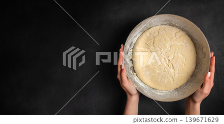 Female hands holding bowl with raw yeast dough on dark background with copy space for homemade baking concept 139671629