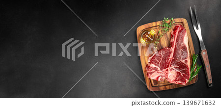 Raw tomahawk beef steak on wooden board with herbs and meat fork on dark background for premium steakhouse advertising 139671632