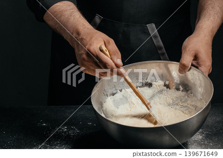 Professional baker mixing sourdough dough in metal bowl in dark kitchen for artisan bakery advertising Professional baker mixing sourdough dough in metal bowl in dark kitchen for artisan bakery advertising 139671649