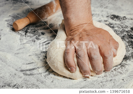 Male baker kneading fresh yeast dough on floured table with rolling pin and copy space for bakery concept 139671658
