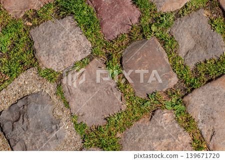 Stone pavement texture with grass between natural paving blocks Stone pavement texture with grass between natural paving blocks 139671720