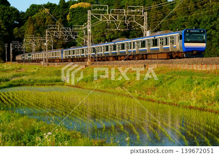 E235 series train running bathed in the setting sun against a backdrop of early summer countryside. E235 series train running bathed in the setting sun against a backdrop of early summer countryside. 139672051
