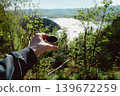 Man holding plastic cup of coffee in forest. Outdoor caffeine boost break with blurred nature background, energy and lifestyle concept 139672259