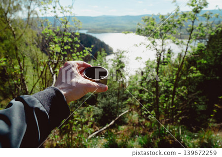 Man holding plastic cup of coffee in forest. Outdoor caffeine boost break with blurred nature background, energy and lifestyle concept Man holding plastic cup of coffee in forest. Outdoor caffeine boost break with blurred nature background, energy and lifestyle concept 139672259