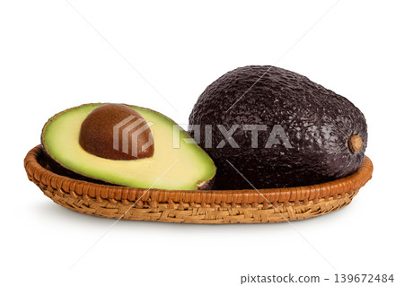 avocado and half in a wicker basket isolated on white background close up 139672484