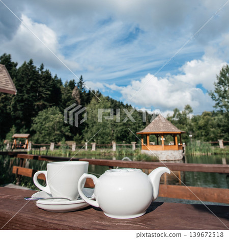Tea cup and teapot on wooden table with lake view in eco resort lifestyle Tea cup and teapot on wooden table with lake view in eco resort lifestyle 139672518