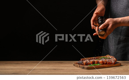 Chef seasoning grilled steak with pepper grinder on dark background with copy space food advertising concept Chef seasoning grilled steak with pepper grinder on dark background with copy space food advertising concept 139672563