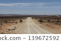 An off-road landscape with a single road cutting through a dry grassland. 139672592