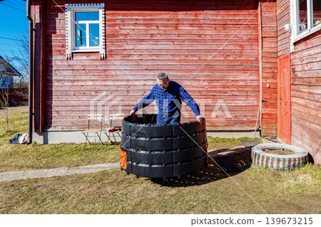 Gardener setting up compost bin by connecting plastic sections outdoors. Gardener setting up compost bin by connecting plastic sections outdoors. 139673215