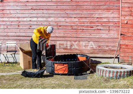 Assembling modular composter from plastic panels female gardener inserts sections into grooves with latch lock 139673222