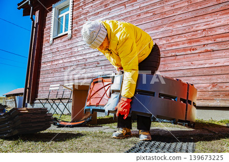 Interlocking compost bin panels being connected into circular structure by woman near country home. Interlocking compost bin panels being connected into circular structure by woman near country home. 139673225