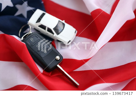 Ignition keys with remote control buttons and toy car on United States flag. Car driving in USA Ignition keys with remote control buttons and toy car on United States flag. Car driving in USA 139673417