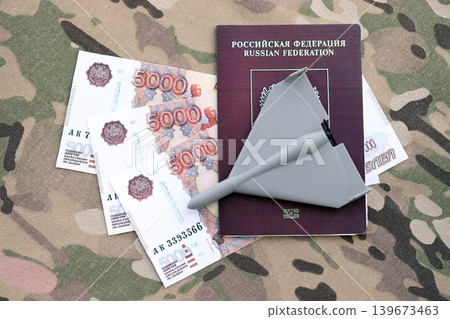 Russian money with bullets and kamikaze drone on passport and multicam camouflage fabric 139673463