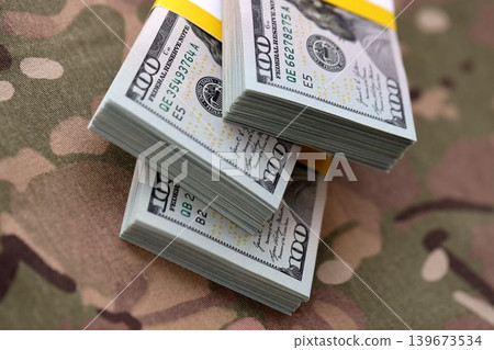 Three packs of ten thousand US dollar bills on camouflage background. Packs of hundred dollar bills Three packs of ten thousand US dollar bills on camouflage background. Packs of hundred dollar bills 139673534