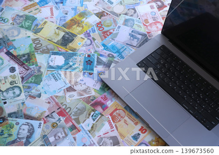 Modern laptop lies on big amount of money bills banknotes from different currencies Modern laptop lies on big amount of money bills banknotes from different currencies 139673560