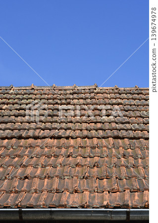 Old weathered clay tile roof with gutter under blue sky Old weathered clay tile roof with gutter under blue sky 139674978