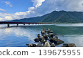 A railway bridge stretching from the mountains and a riverside landscape with clouds spreading across the horizon. 139675955