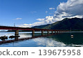 A wide view of a railway bridge crossing a river and mountains. 139675958
