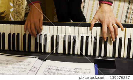 Top view of adult female hands playing gentle piece of classical music on black piano. Scene captures the movement, rhythm and elegance of performance, highlighting beauty of live instrumental play 139676287
