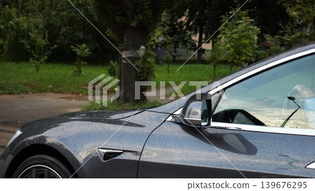 Businessman in shirt driving a modern electric car at sunny rainy day. Male successful entrepreneur riding on electrical vehicle at city. Young manager commuting to work at urban road. Slow motion Businessman in shirt driving a modern electric car at sunny rainy day. Male successful entrepreneur riding on electrical vehicle at city. Young manager commuting to work at urban road. Slow motion 139676295