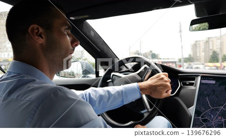 Handsome businessman driving a modern electric car at urban road. Male successful entrepreneur riding on electrical vehicle at rain city. Young man commuting to work at rainy day. Slow mo 139676296