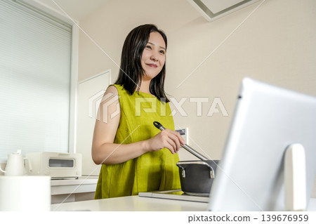 A woman cooking while checking a recipe on a tablet. A woman cooking while checking a recipe on a tablet. 139676959