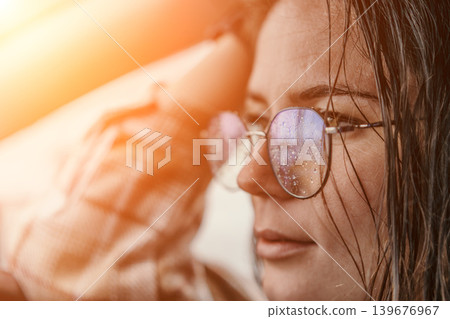 Woman glasses raindrops standing with wet hair and eyeglasses covered in moisture during a warm orange sunset glow 139676967