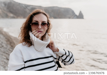 Woman seascape fashion portrait of elegant lady in striped sweater and sunglasses standing on rocky coast with cliffs and copy space Woman seascape fashion portrait of elegant lady in striped sweater and sunglasses standing on rocky coast with cliffs and copy space 139676976