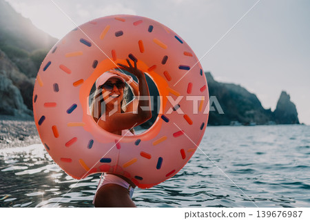 Young woman donut float ocean smiles through inflatable donut on summer vacation with copy space. Young woman donut float ocean smiles through inflatable donut on summer vacation with copy space. 139676987