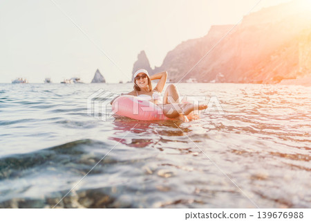 Woman, ocean, relaxation, happy female enjoying summer vacation on pink inflatable ring in serene sea with cliffs. Woman, ocean, relaxation, happy female enjoying summer vacation on pink inflatable ring in serene sea with cliffs. 139676988