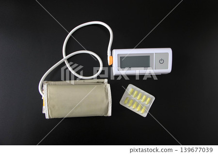 Digital blood pressure monitor with cuff and pills on black background Digital blood pressure monitor with cuff and pills on black background 139677039