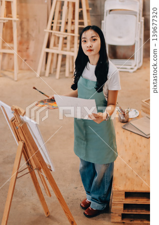 Female artist wears black hat posing near picture indoor the studio Female artist wears black hat posing near picture indoor the studio 139677320