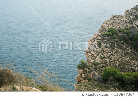 Majestic cliffside overlooking the tranquil sea with lush greenery and rocky terrain 139677364
