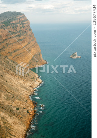 Majestic coastal cliffs and rock formation against expansive ocean and cloudy sky Majestic coastal cliffs and rock formation against expansive ocean and cloudy sky 139677434