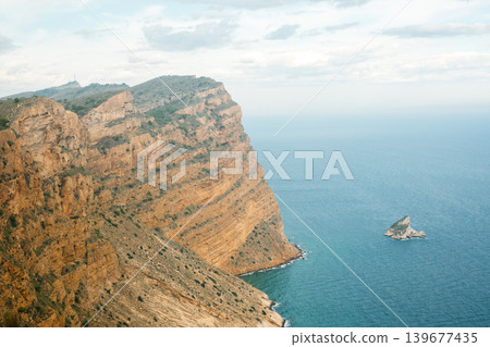 Majestic coastal cliff with rocky outcrop and expansive ocean views under cloudy sky Majestic coastal cliff with rocky outcrop and expansive ocean views under cloudy sky 139677435